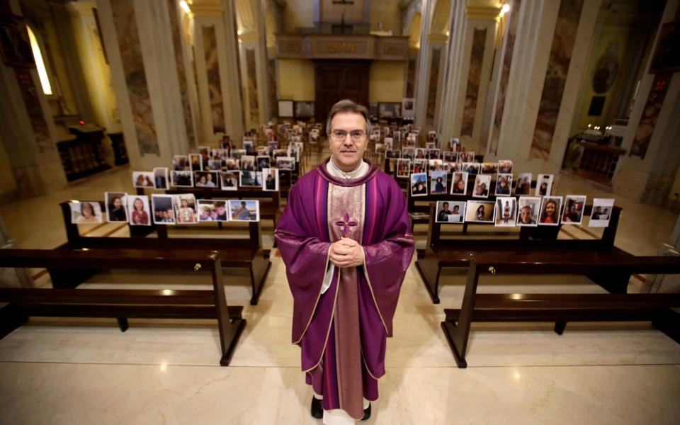 Don Giuseppe Corbari, poses in front of selfies he was sent by parishioners - AP Photo/Luca Bruno