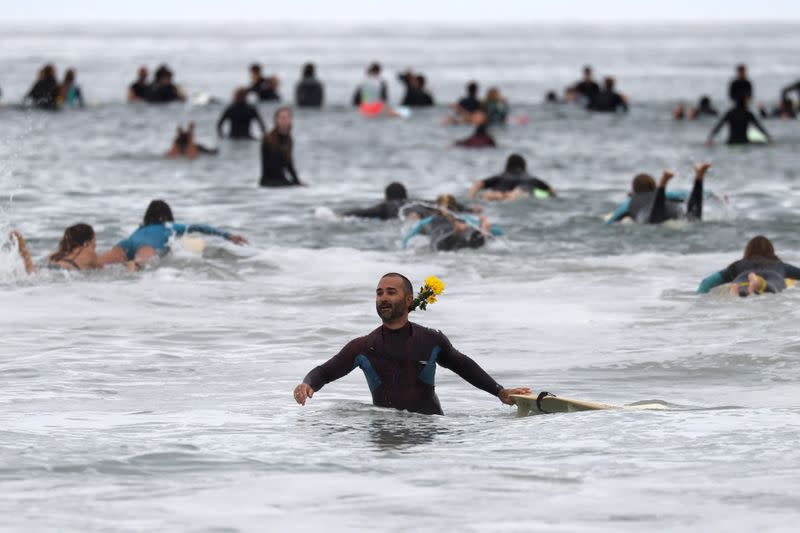 A man carries a flower into the ocean at The Black Girls Surf paddle-out in memory of George Floyd, who died in Minneapolis police custody, in Santa Monica