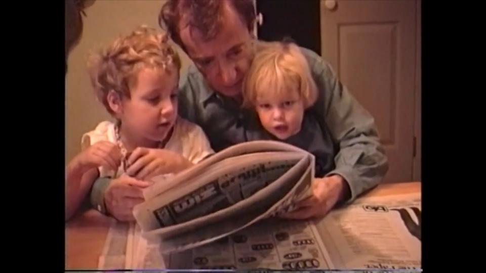 Young Dylan and Ronan Farrow sit in Woody Allen's lap, looking at a newspaper.