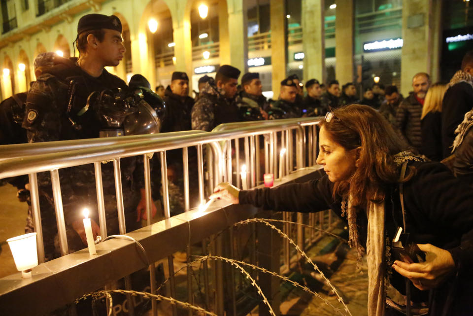 An anti-government protester lights a candle in front the riot police, during ongoing protests against the ruling elite of corruption and financial crisis, in downtown Beirut, Lebanon, Wednesday, Dec. 18, 2019. Lebanon's caretaker prime minister said Wednesday he's no longer a candidate for the post, eliminating himself from consideration on the eve of scheduled consultations between the president and parliamentary blocs for naming a new premier. (AP Photo/Hussein Malla)