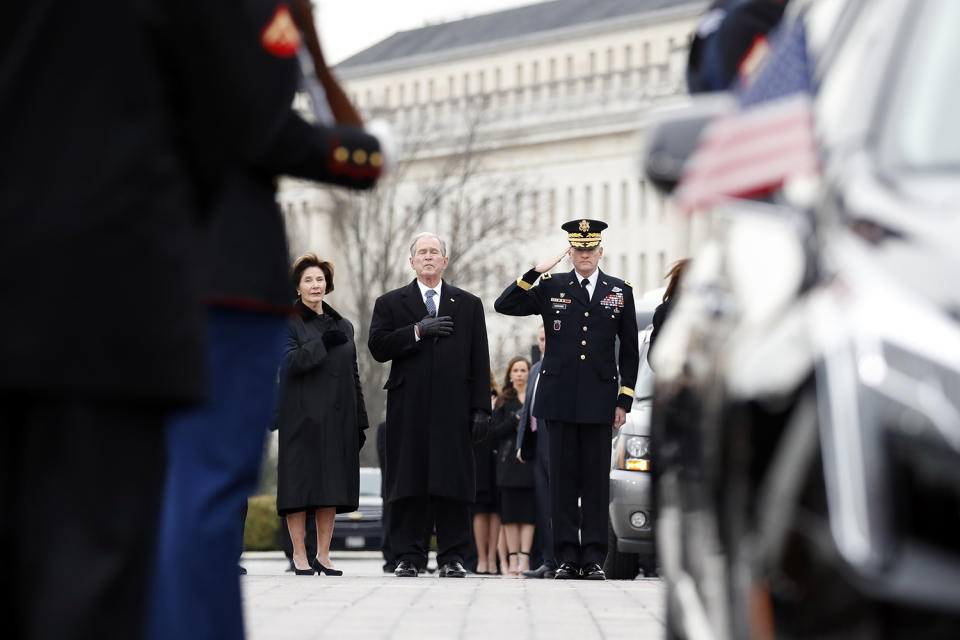 Former President George W. Bush and former first lady Laura Bush put their hands over their hearts as a joint services military honor guard carries the flag-draped casket of former President George H. W. Bush from the U.S. Capitol to transport it to Washington National Cathedral, Dec. 5, 2018 in Washington, D.C. (Photo: Alex Brandon – Pool/Getty Images)