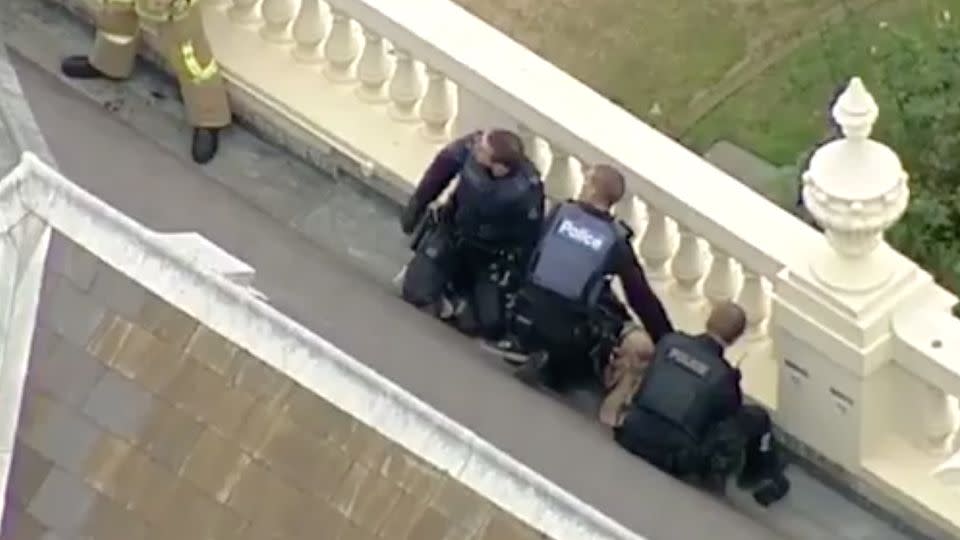 Chopper footage showed the man handcuffed and detained by three police officers on the roof of Melbourne's Government House. Source: 7 News