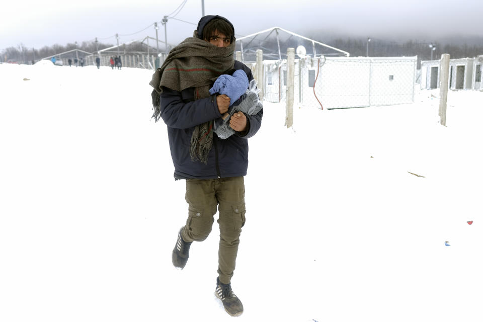 A migrant carries footwear and blankets received from humanitarian organization at the Lipa camp, outside Bihac, Bosnia, Monday, Jan. 11, 2021. Aid workers say migrants staying at a camp in northwestern Bosnia have complained or respiratory and skin diseases after spending days in make-shift tents and containers amid freezing weather and snow blizzards. Most of the hundreds of migrants at the Lipa facility near Bosnia's border with Croatia on Monday have been accommodated in heated military tents following days of uncertainty after a fire gutted most of the camp on Dec. 23. (AP Photo/Kemal Softic)