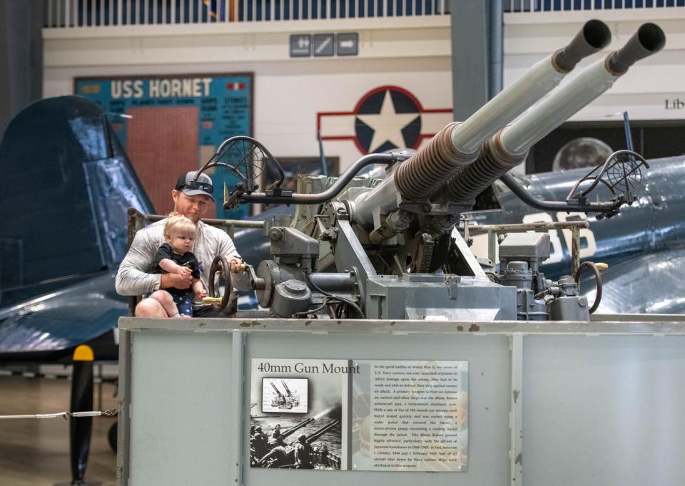 Matt Blank holds his daughter Haddie as they check out a 40 mm gun mount while touring the National Naval Aviation Museum. The museum will host a night of the Navy Days Celebration.