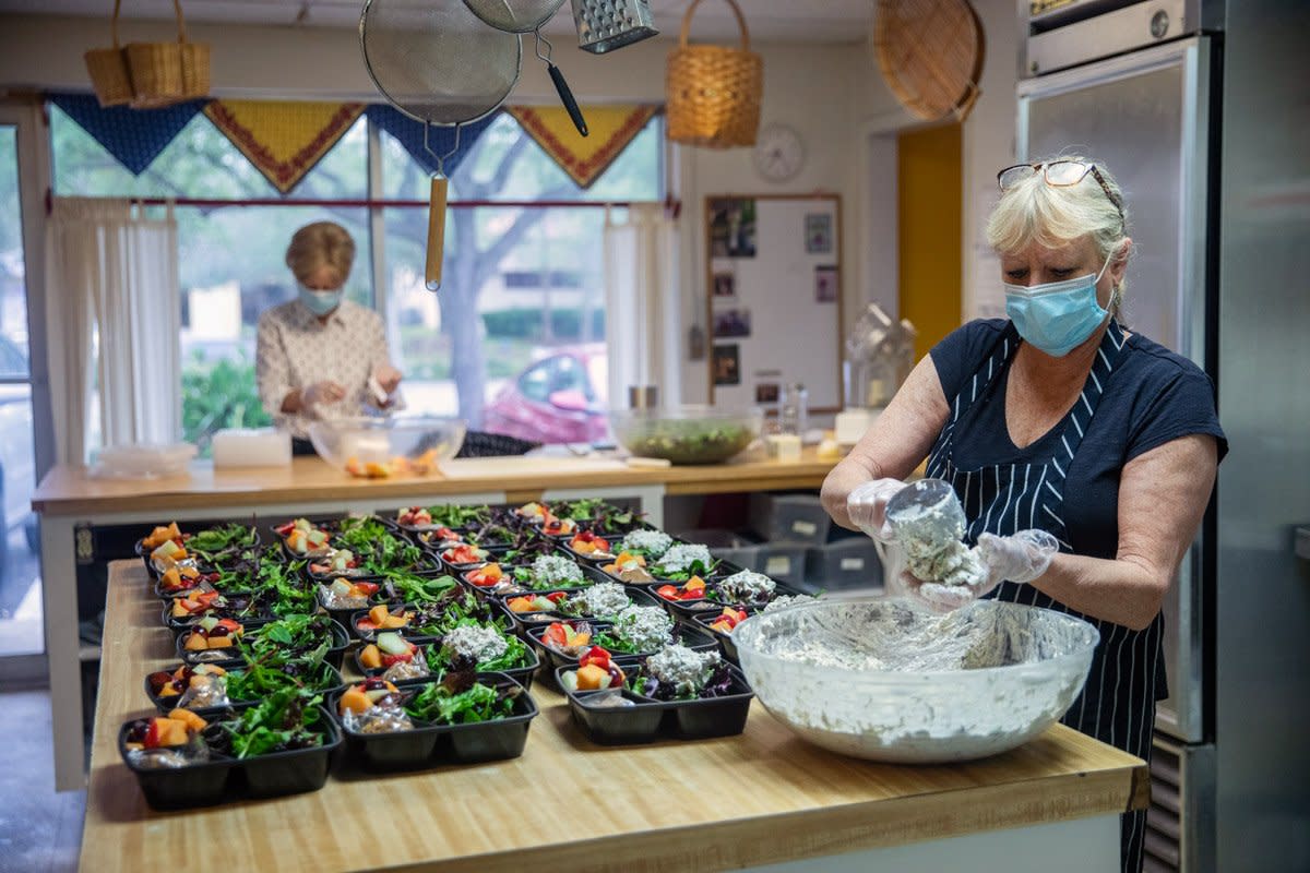 A woman scoops up potato salad into individually wrapped prepared lunches for her customers. 