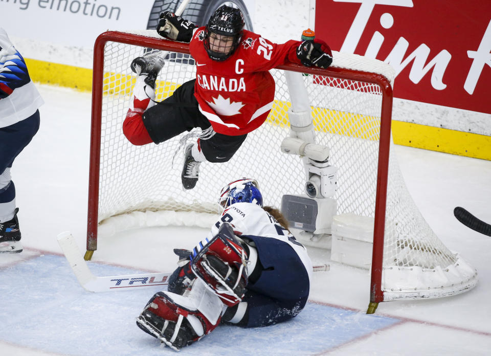 Canada's Marie-Philip Poulin, top, hangs from the cross bar after crashing into U.S. goalie Nicole Hensley during the third period of the IIHF hockey women's world championships title game in Calgary, Alberta, Tuesday, Aug. 31, 2021. (Jeff McIntosh/The Canadian Press via AP)