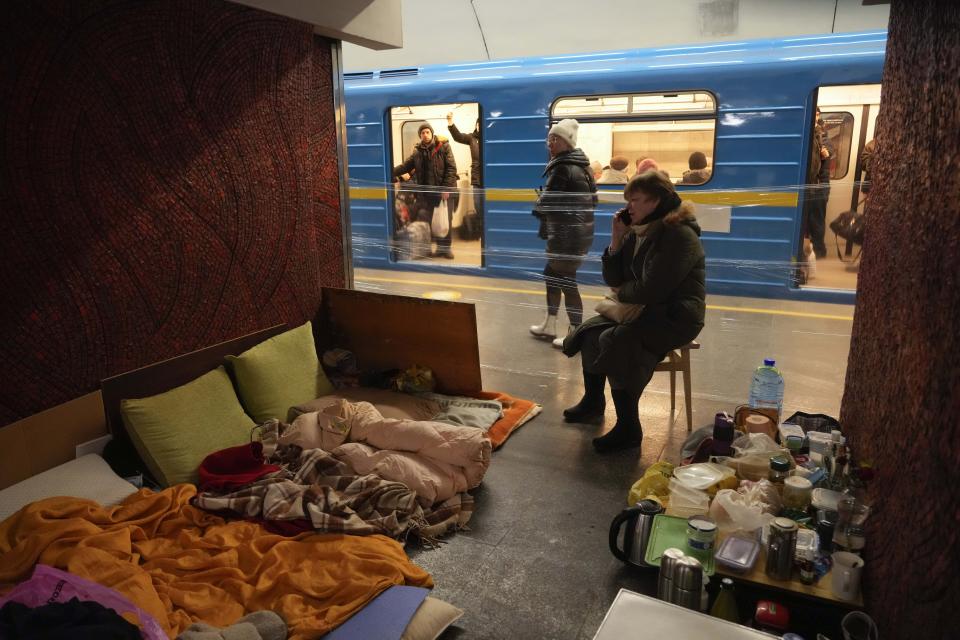 A woman with her belongings and food, sits on a chair in an improvised shelter in a subway that city residents use as a bomb shelter while a train passes by in the opposite line in Kyiv, Ukraine, Sunday, March 13, 2022. (AP photo/Efrem Lukatsky)