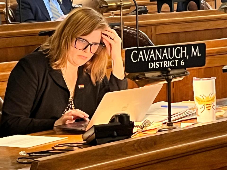 State Sen. Machaela Cavanaugh looks down at her white laptop while sitting behind a brown desk with a black placard that has her name on it