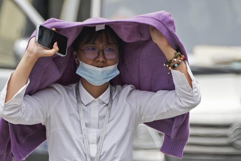 A woman uses a sweater to shield from the sun as she walls on a street on a hot day in Beijing, Monday, July 3, 2023. Heavy flooding has displaced thousands of people around China as the capital had a brief respite from sweltering heat. Beijing reported 9.8 straight days when the temperature exceeded 35 C (95 F), the National Climate Center said Monday. (AP Photo/Andy Wong)