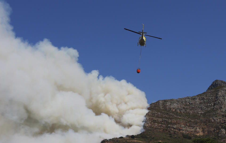 A helicopter drops water over a fire at Rhodes Memorial on Table Mountain, Cape Town, South Africa, Sunday, April 18, 2021. A wildfire raging on the slopes of the mountain forced the evacuation of students from the University of Cape Town. (AP Photo/Nardus Engelbrecht)