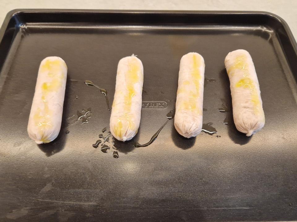 four frozen sausage links on a baking tray with oil