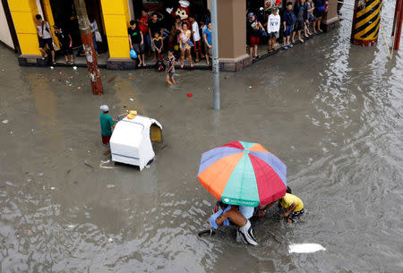 People stand along a sidewalk as they watch commuters manoeuvre their pedicabs along floodwaters in Las Pinas, Metro Manila as a storm sweeps across the main Luzon island, Philippines, September 12, 2017. REUTERS/Erik De Castro