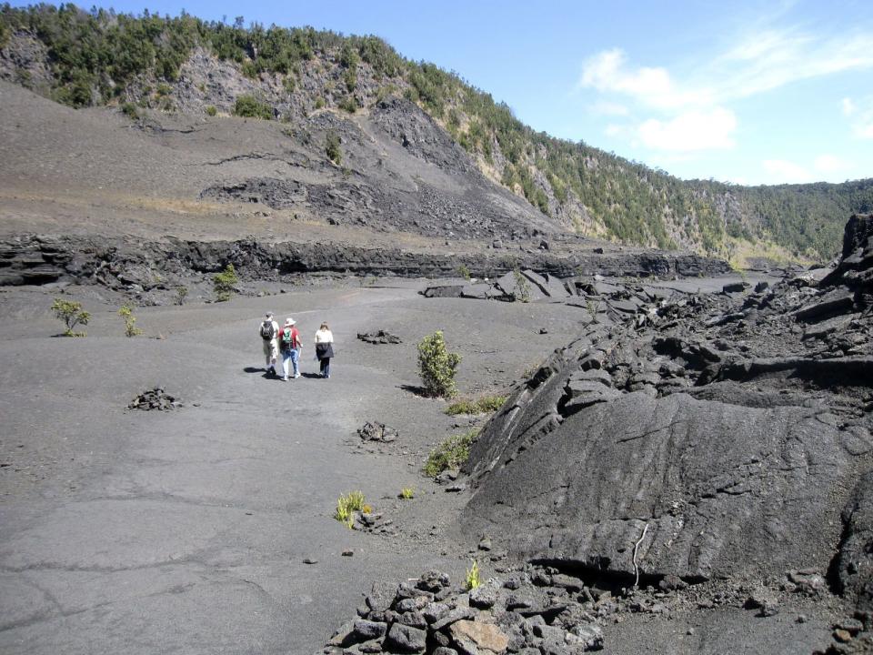 This Feb. 15, 2010, photo shows tourists as they walk across the floor of the Kilauea volcano in Hawaii Volcanoes National Park on the Big Island. Hikes in the park offer an astonishing contrast of landscapes, from a lush rainforest to the black crater to the sea. | Beth Harpaz, Associated Press