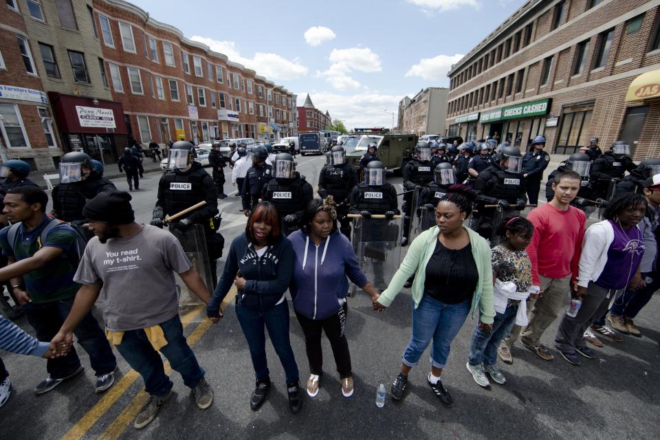 People clasp hand and sing the hymn "Amazing Grace" Tuesday, April 28, 2015, in Baltimore, in the aftermath of rioting following Monday's funeral for Freddie Gray, who died in police custody. The streets were largely calm in the morning and into the afternoon, but authorities remained on edge against the possibility of another outbreak of looting, vandalism and arson. (AP Photo/Matt Rourke)