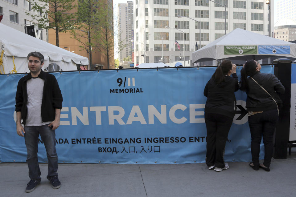 A visitor to the Sept. 11 Memorial, left, poses for a photo as others, right, peer at the entrance line, Saturday, May 4, 2013, in New York. Faced with hefty operating costs, the foundation building the underground 9/11 museum at the World Trade Center has decided to charge a mandatory admission fee of $20 to $25 when the site opens next year. Entry to the memorial plaza with its twin reflecting pools will still be free, but the decision to charge for the underground museum housing relics of the terror attacks has been greeted with dismay by some relatives of trade center victims. (AP Photo/Mary Altaffer)