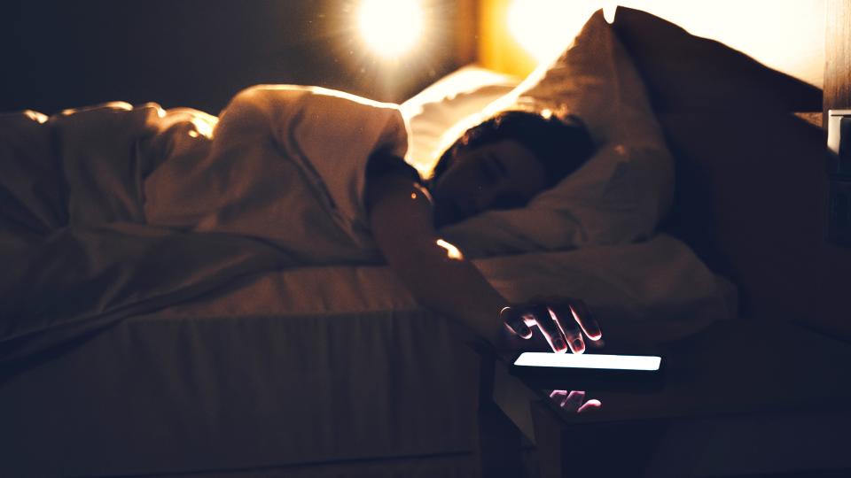 Morning shot of a person lying in bed tapping phone, turning off the alarm