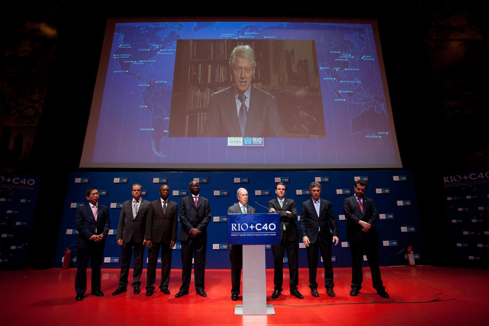 A live image of former President Bill Clinton is projected as he speaks with mayors, from left to right, Won Soon Park of Seoul, Ecktar Wuerzner of Heidelberg, Babatunde Fashola of Lagos, Franklyn Tau of Johannesburg, Michael Bloomberg of New York, Eduardo Paes of Rio de Janeiro, Eduardo Macri of Buenos Aires and Eduardo Kassab of Sao Paulo, during the Rio+C40 meeting, a parallel event during the UN Conference on Sustainable Development, or Rio+20, in Rio de Janeiro, Brazil, Tuesday, June 19, 2012. While squabbling between rich and poor countries threatens to derail the Earth summit, the world’s mayors say they can’t afford the luxury of endless, fruitless negotiations and are already taking real action to stave off environmental disaster and preserve natural resources for future generations. (AP Photo/Felipe Dana)