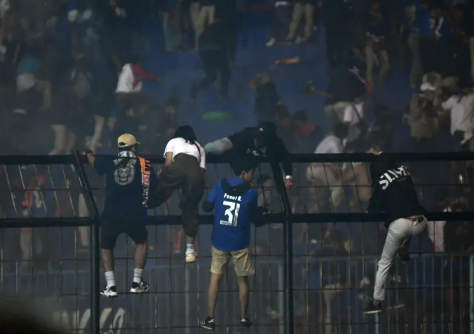 Spectators climb a fence by the stands amid a deadly stampede after a football match at Kanjuruhan Stadium in Malang, East Java, Indonesia, on Oct. 1, 2022.