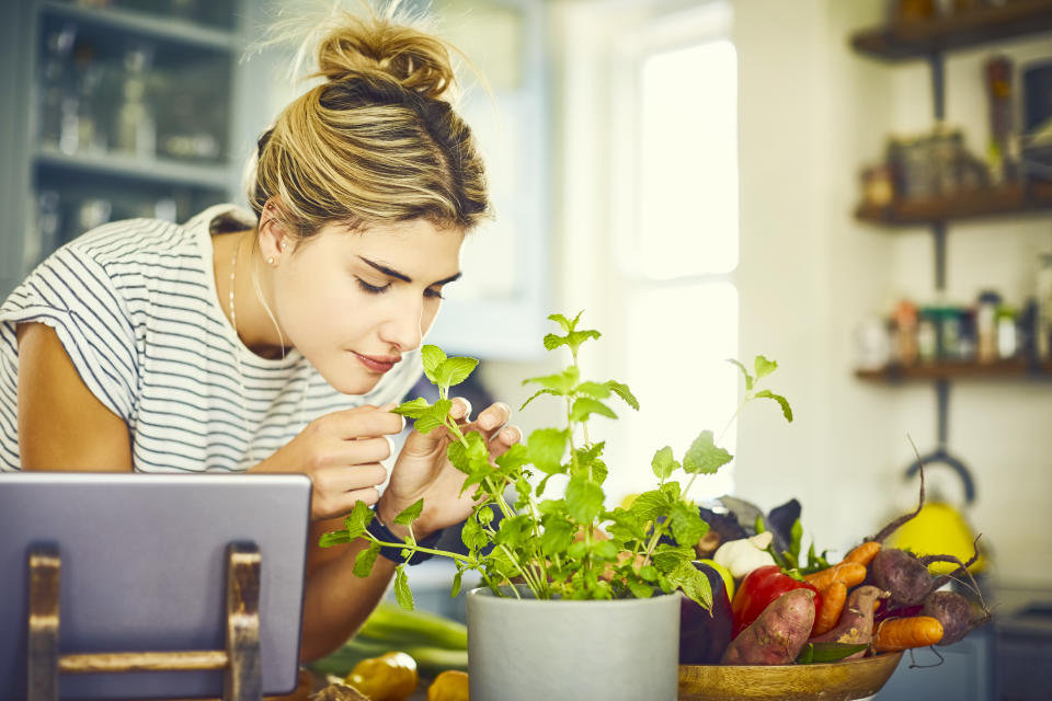 Young woman smelling mint leaves by digital tablet. Female is preparing food from recipe on tablet. She is in trendy casuals.