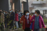 Women wearing face masks to help curb the spread of the coronavirus chat each other as they walk by masked residents line up to receive booster shots against COVID-19 at a vaccination site in Beijing, Monday, Oct. 25, 2021. A northwestern Chinese province heavily dependent on tourism closed all tourist sites Monday after finding new COVID-19 cases. (AP Photo/Andy Wong)