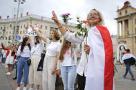 Belarusian opposition supporters hold flowers and flash victory signs during a protest in Victory Square in Minsk, Belarus, Thursday, Aug. 20, 2020. Demonstrators are taking to the streets of the Belarusian capital and other cities, keeping up their push for the resignation of the nation's authoritarian leader. President Alexander Lukashenko has extended his 26-year rule in a vote the opposition saw as rigged. (AP Photo/Sergei Grits)