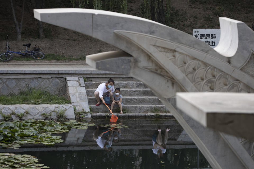 A woman and a child wear masks to curb the spread of the coronavirus as they use a net to look for fish along a canal in Beijing Saturday, June 20, 2020. China's capital recorded a further drop in coronavirus cases amid tightened containment measures. (AP Photo/Ng Han Guan)
