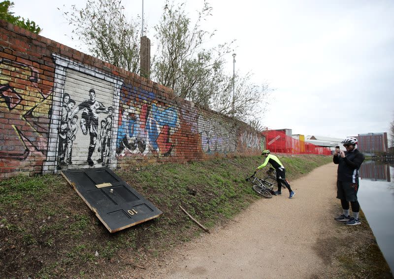 A man takes a photo of a mural of England soccer player Marcus Rashford kicking down the door of number 10 Downing Street on Manchester Canal in Manchester