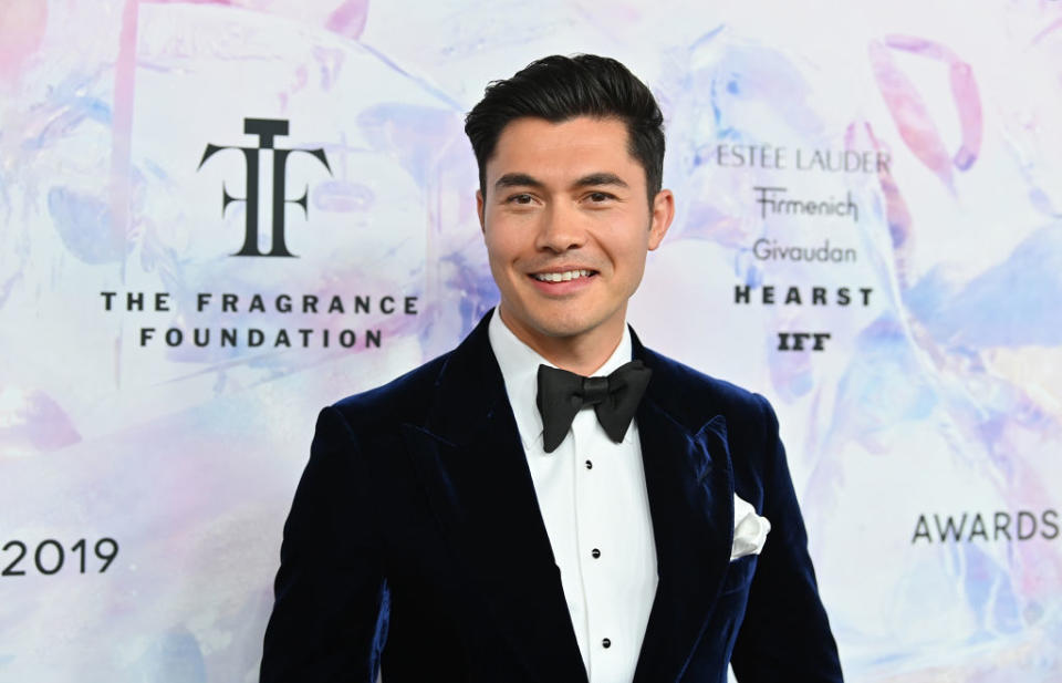 Henry Golding in a tuxedo with a bow tie at The Fragrance Foundation Awards. Logos and words in background reference the event and sponsors