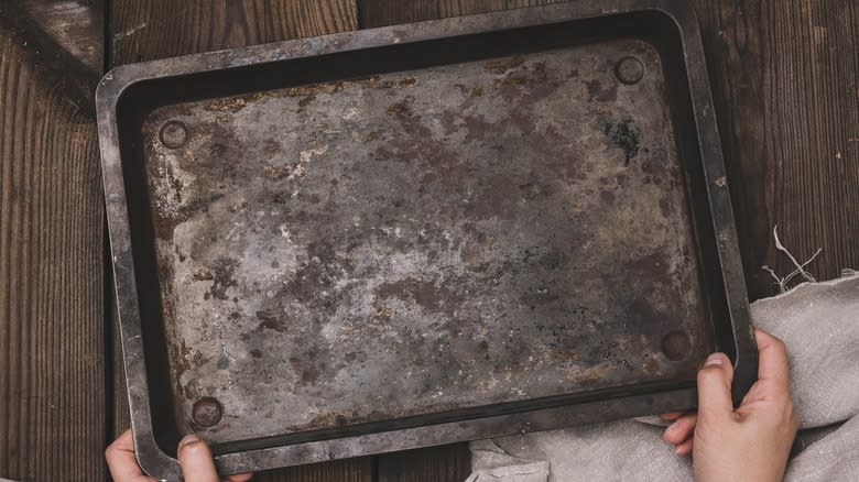 hands holding rusty baking sheet