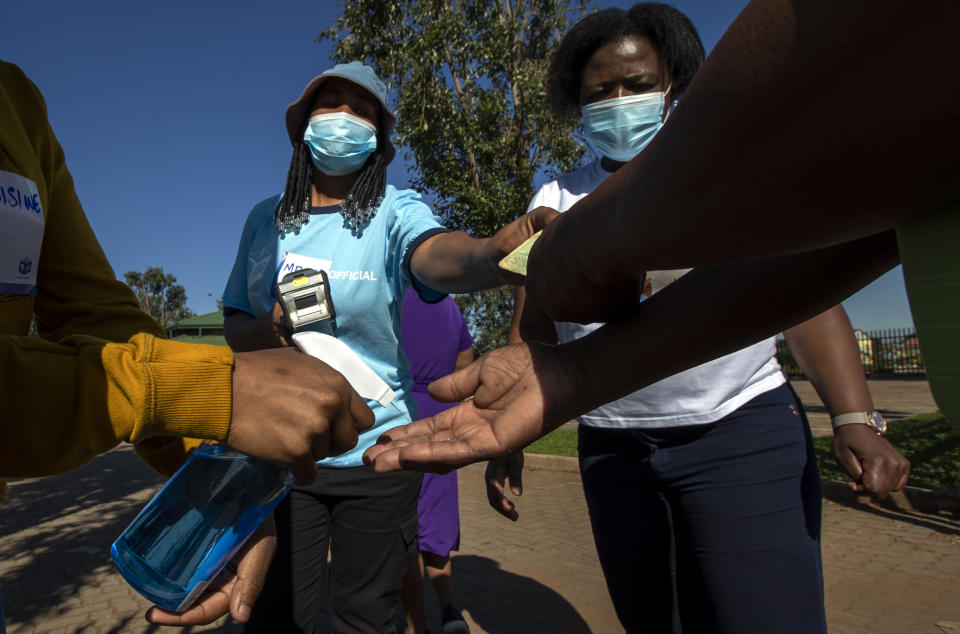 A member of the electoral commission sanitizes voters at the entrance of a polling station in Thokoza, east of Johannesburg, Monday, Nov. 1, 2021. South Africa is holding crucial local elections Monday. (AP Photo/Themba Hadebe)