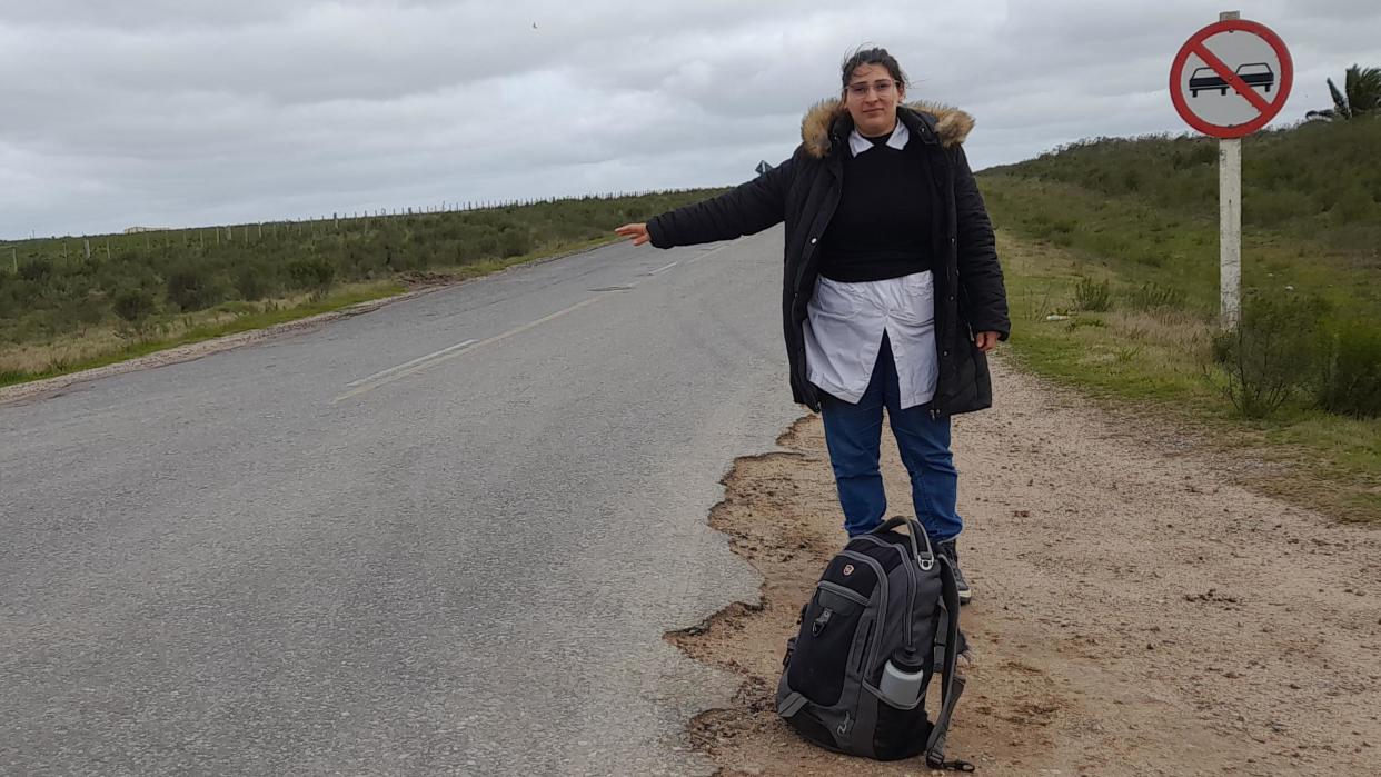 La maestra María Domínguez al borde de la carretera extiende su brazo en señal de que pide un aventón.