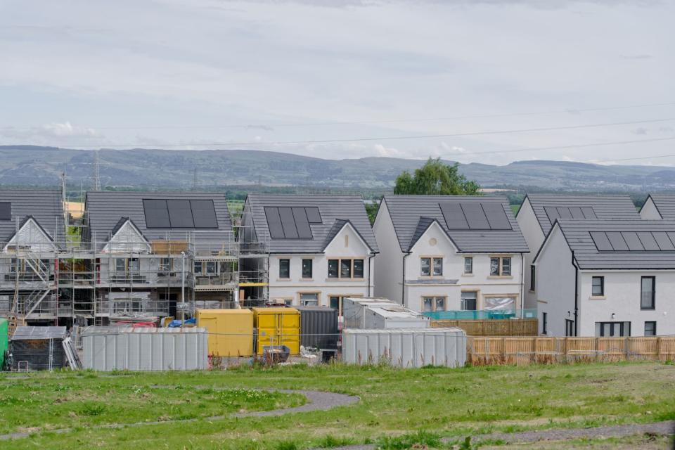 A row of homes against a mountainous backdrop have solar panels on their roofs.