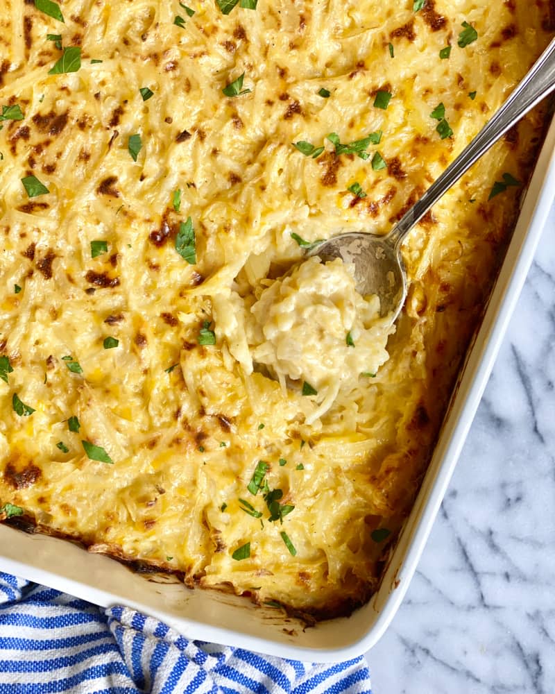 Potato casserole in a white baking dish, with a spoon resting inside, on a white marble surface