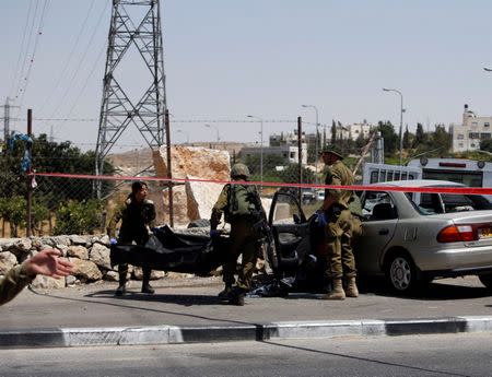 Israeli soldiers remove the dead body of a Palestinian assailant at the scene of a car-ramming attack at the entrance of Beit Einun village, near the West Bank City of Hebron July 18, 2017. REUTERS/Mussa Qawasma