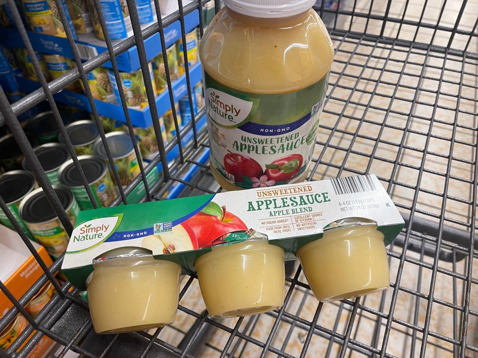 A jar and small packs of Simply Nature unsweetened applesauce in a shopping cart.