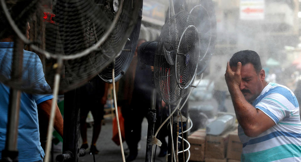 A man stands by fans spraying air mixed with water vapour deployed by donors to cool down pedestrians along a street in Iraq's capital Baghdad on June 30, 2021 amidst a severe heat wave. (Photo by AHMAD AL-RUBAYE / AFP) (Photo by AHMAD AL-RUBAYE/AFP via Getty Images)