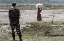 A villager carries her belongings and walks past a paramilitary soldier as she flees her violence-affected village of Narayanguri, in the northeastern Indian state of Assam, Saturday, May 3 2014. Police in India arrested 22 people after separatist rebels went on a rampage, burning homes and killing dozens of Muslims in the worst outbreak of ethnic violence in the remote northeastern region in two years, officials said Saturday. (AP Photo/Anupam Nath)