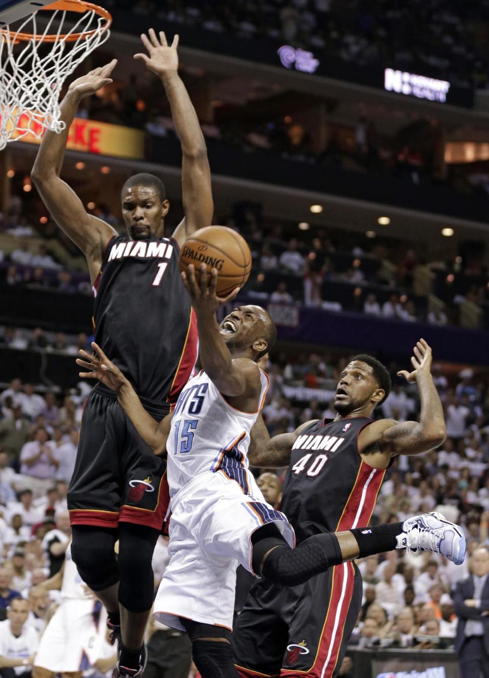 Charlotte Bobcats' Kemba Walker (15) is fouled as he drives between Miami Heat's Chris Bosh (1) and Udonis Haslem (40) during the first half in Game 3 of an opening-round NBA basketball playoff series in Charlotte, N.C., Saturday, April 26, 2014. (AP Photo/Chuck Burton)