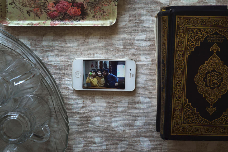 This Aug. 23, 2018, photo, shows a phone displaying an image of three of Meripet's children, now in a live-in kindergarten in China, on a table surrounded by tea glasses and a Quran in her home in Istanbul, Turkey. Meripet came to Turkey in February 2017 to visit her sick father, leaving four children behind. While in Turkey, she heard Uighur passports were being seized and that people who had gone abroad were being taken to reeducation – so she stayed in Turkey, giving birth to Abduweli. She hasn't seen her other four children since, and heard they were taken to a live-in kindergarten in Hotan, China. (AP Photo/Dake Kang)