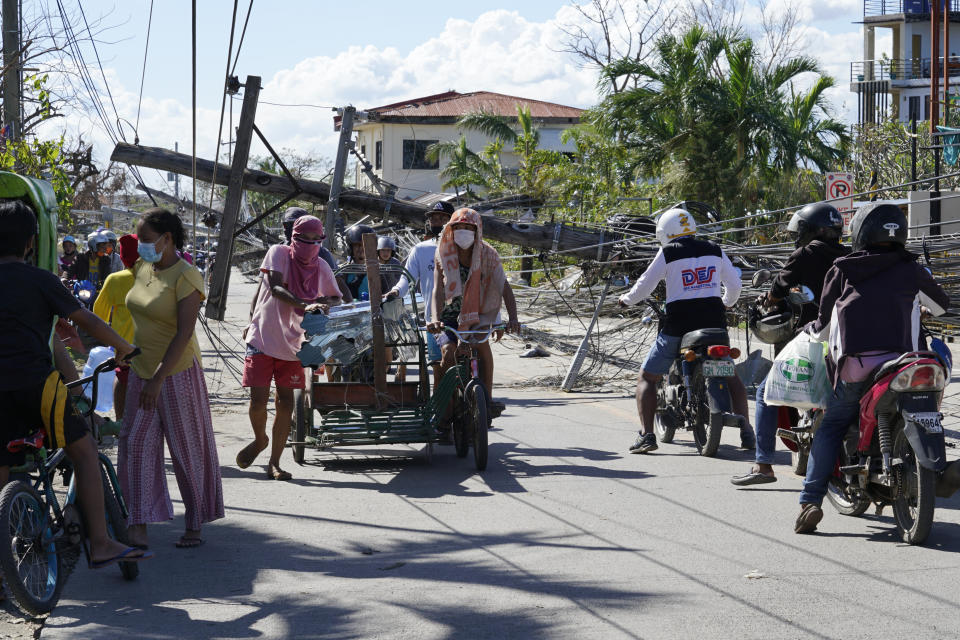 Residents pass by toppled electrical posts due to Typhoon Rai in Cebu province, central Philippines on Monday Dec. 20, 2021. The death toll in the strongest typhoon to batter the Philippines this year continues to rise and the governor of an island province especially hard-hit by Typhoon Rai said there may be even greater devastation that has yet to be reported. (AP Photo/Jay Labra)