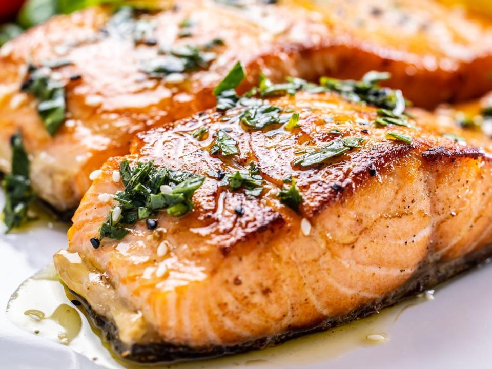 Two cooked fillets of salmon on a plate with salad in the background.