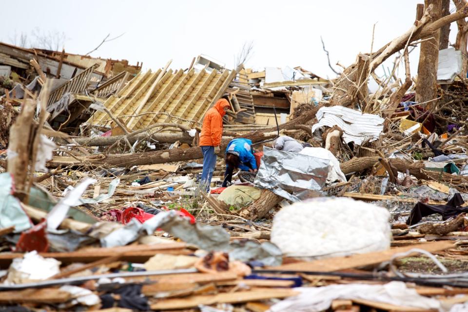 Two men looking through building debris left after a tornado.