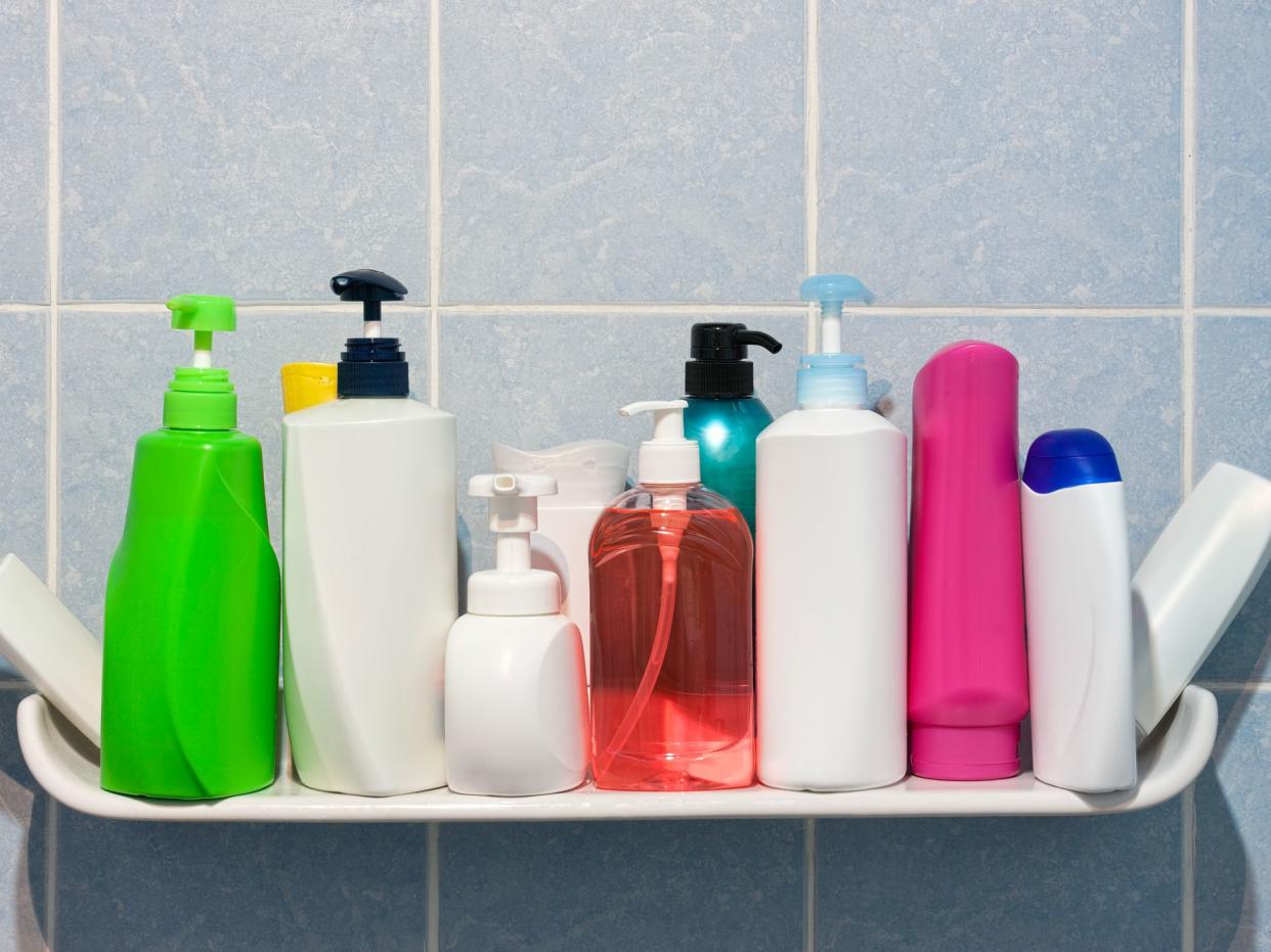 Many shampoo and soap bottles on a bathroom or shower shelf.