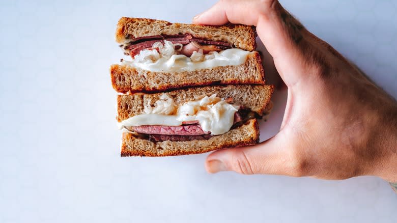 Hand holding two halves Reuben sandwich