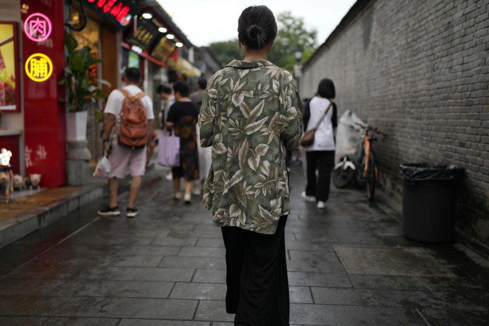 Financial analyst Megan Ji, who asked not to show her face fearing repercussions from her company, walks down a busy alleyway in Beijing, Sunday, Aug. 20, 2023. At an office karaoke party, Ji surprised her colleagues when she told her supervisor to stop caressing her back. She credits Japanese scholar Chizuko Ueno with introducing her to ideas of feminism. (AP Photo/Ng Han Guan)