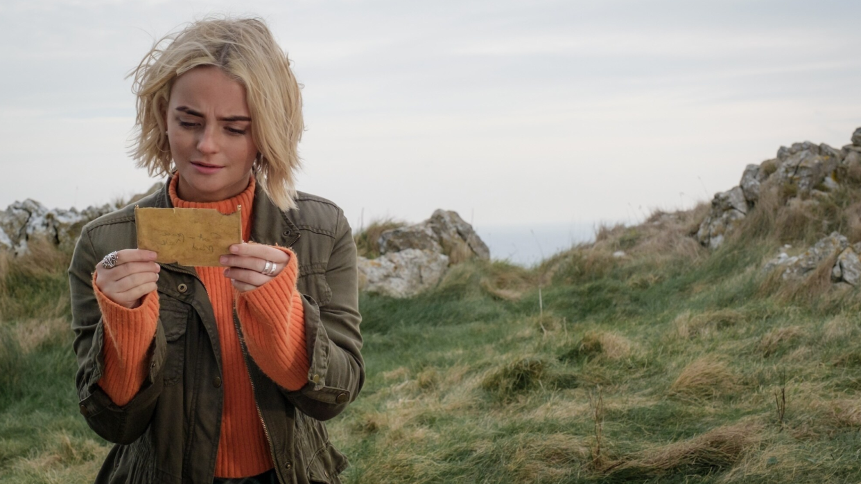  Millie Gibson as Ruby Sunday in Doctor Who looks down at a piece of paper on a remote cliff in Wales. 