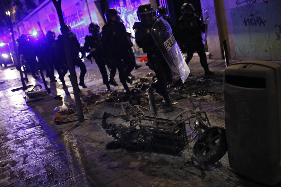 Los antidisturbios pasan junto a una motocicleta completamente calcinada (AP).