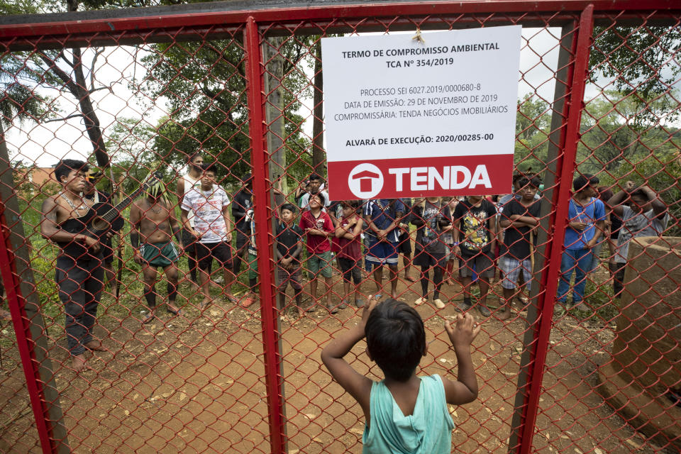 Guarani Mbya protesters stand on both sides of a fence that marks the permitter of a development project for apartment buildings by real estate company Tenda, next to their indigenous community's land in Sao Paulo, Brazil, Thursday, Jan. 30, 2020. The tension between a builder with projects in nine Brazilian states and a 40-family indigenous community is a microcosm of what’s playing out elsewhere in the country. (AP Photo/Andre Penner)