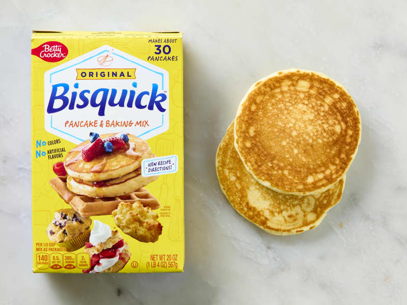 overhead shot of a box of bisquick pancake mix, with two pancakes to the right of it.