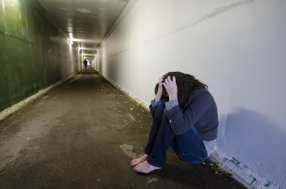 Crime scene concept photo of rape victim. A sad woman sits on the floor of a dark tunnel.